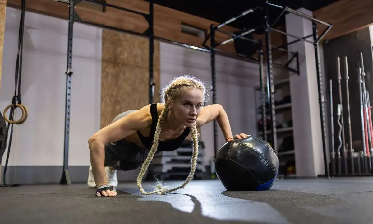 Kobieta wykonuje pompki z piłką w siłowni. Zastanawiasz się, crossfit jak często ćwiczyć, by osiągnąć takie rezultaty?