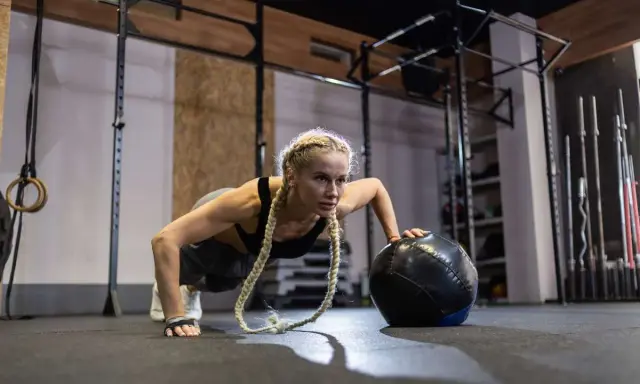 Kobieta wykonuje pompki z piłką w siłowni. Zastanawiasz się, crossfit jak często ćwiczyć, by osiągnąć takie rezultaty?