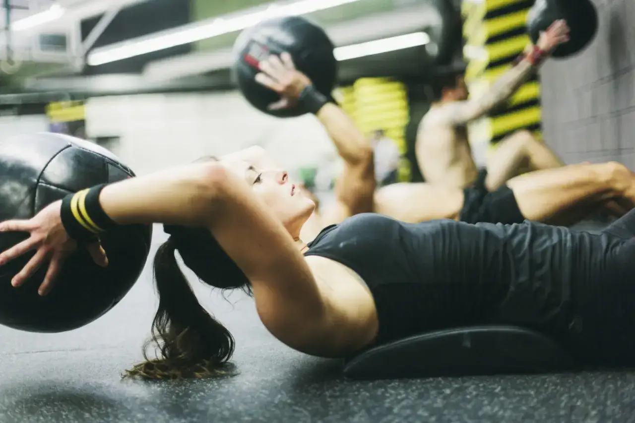 Kobieta wykonuje ćwiczenia brzucha z piłką lekarską. Często ćwiczy crossfit, budując siłę.